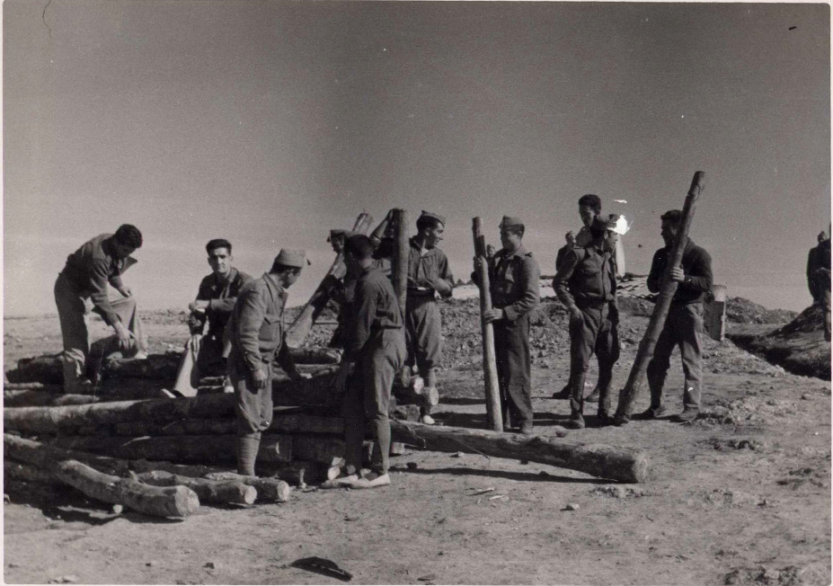 foto en la que se ven a 10 soldados portando postes de madera para la construcción de un albergue.
