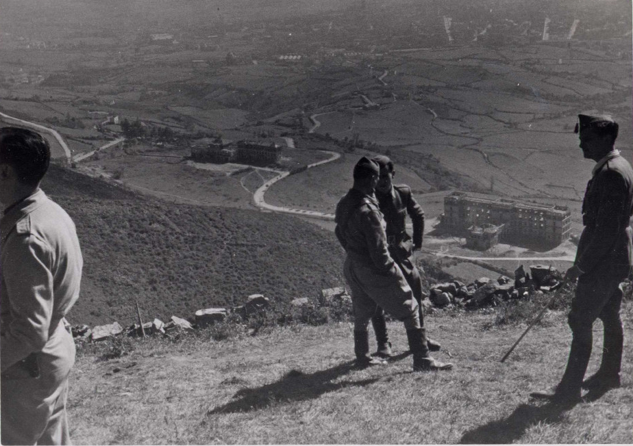 foto de 4 oficiales que hablan entre ellos. Al fondo y a sus pies se ve el sanatorio del Monte Naranco.