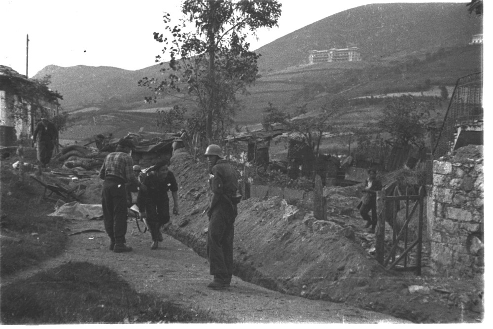 foto en la que se ve a 3 milicianos de pies y a otros corriendo para retirarse de un parapeto