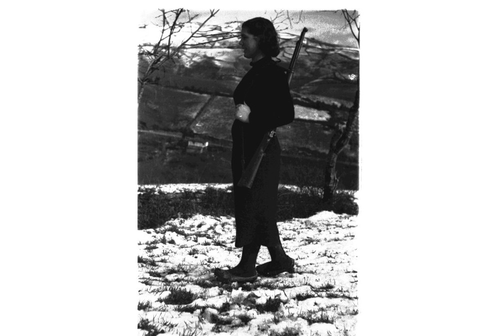foto de una joven miliciana con madreñas y un fusil. Al fondo un paisaje nevado.